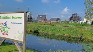 Ein Schild mit Text und Logos, ein Teich mit Seerosen und Häuser im Hintergrund.