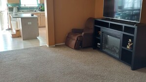 A living room with a TV, a fireplace, and a kitchen visible through an open doorway.
