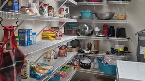 A kitchen with multiple shelves stocked with various food items, kitchenware, and appliances.