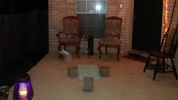 A room with a brick wall, a window, two armchairs, a small table, and a heater.