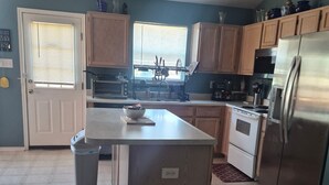 A kitchen with wooden cabinets, a stainless steel refrigerator, and a window with blinds.