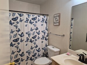 Une salle de bain équipée d’une douche avec un rideau de douche orné d’un motif de papillons, de toilettes, d’un lavabo avec un miroir et d’une étagère fixée au mur.