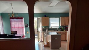 A view through an archway into a room with a dining table, chairs, and a window with curtains.