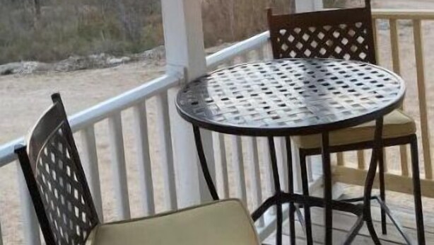 A covered outdoor area with a round metal table and two chairs, overlooking a landscape with trees and a sunset. - Cowboy Sunset at the Orrasis (Marble Falls)