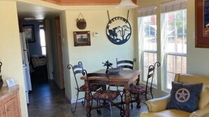 A spacious living area with a high ceiling, a wooden staircase, a dining table with chairs, a leather sofa, and a cowhide rug. - Cowboy Sunset at the Orrasis (Marble Falls)