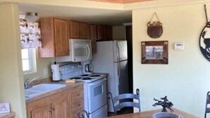 A compact kitchen with wooden cabinets, a microwave, a stove, and a refrigerator. There is a dining table with chairs and a decorative bowl on it. - Cowboy Sunset at the Orrasis (Marble Falls)