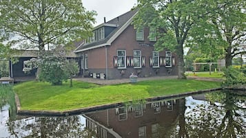 A two-story brick house with a sloped roof, a small front garden, and a pond in the foreground.