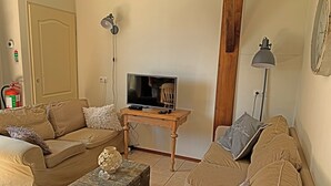 A living room with a television on a wooden stand, a sofa, a small table with a decorative item, and a lamp. - Christinahoeve Oude Deel #4 (Boskoop)