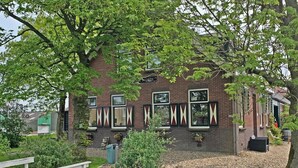 A brick building with multiple windows, a wooden deck, and a small garden area. - Christinahoeve Oude Deel #4 (Boskoop)