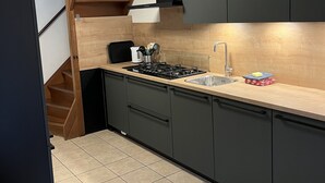 A modern kitchen with dark cabinets, a wooden staircase, and a tiled floor. - Christinahoeve Oude Deel #4 (Boskoop)