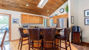 A kitchen with wooden cabinets, a refrigerator, a microwave, and a dining area with leather chairs. - WITC03 - Updated Home, Great Outdoor Space, AC, Hot Tub (Sunriver)