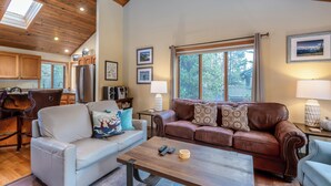 A living room with a sofa, a coffee table, and a couch. There is a kitchen area in the background with wooden cabinets and a refrigerator. - WITC03 - Updated Home, Great Outdoor Space, AC, Hot Tub (Sunriver)