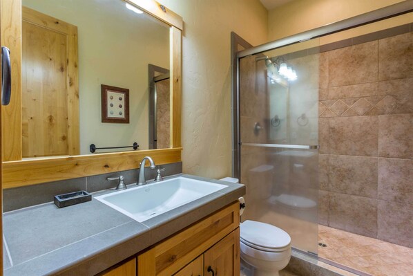 A bathroom with a wooden vanity, a white sink, a mirror, and a glass-enclosed shower. - JACK10 - Spacious Home, 5 Suites, Foosball, Private Hot Tub, Bikes (Sunriver)