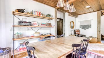 Cozy dining area with a long table and four chairs, surrounded by shelves and a woven basket.