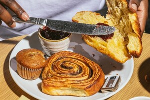 Un plato con un muffin, un rollo de canela y una rebanada de pan con mermelada.