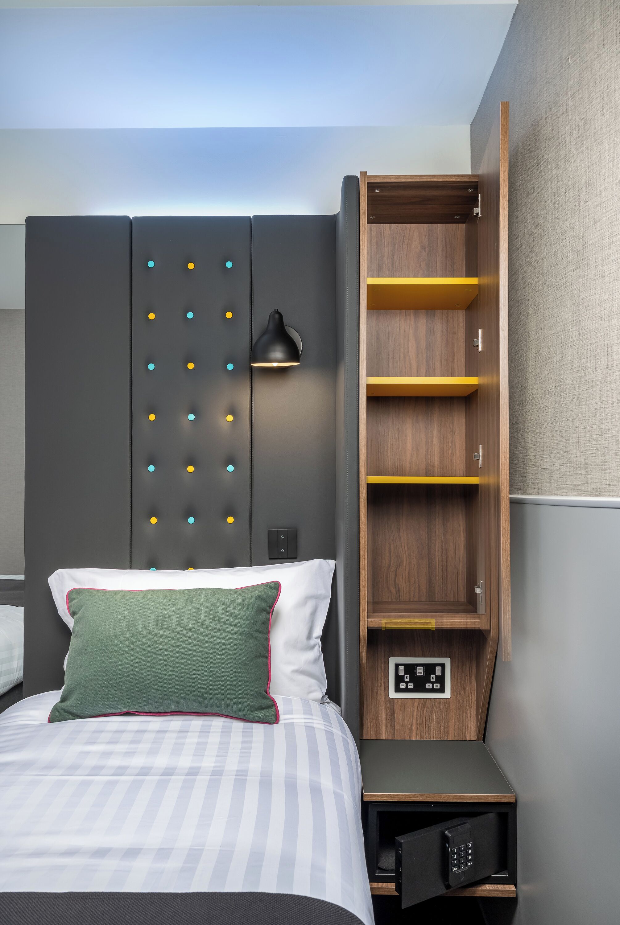 Een hotelkamer met een bed, een kledingkast met een verlichtingspaneel, en een nachtkastje met een bedieningspaneel.