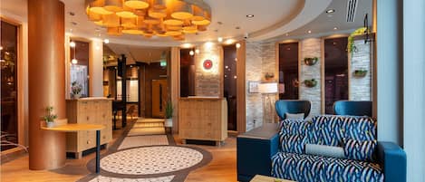 A modern lobby with a central seating area, wooden reception desk, and a patterned floor.