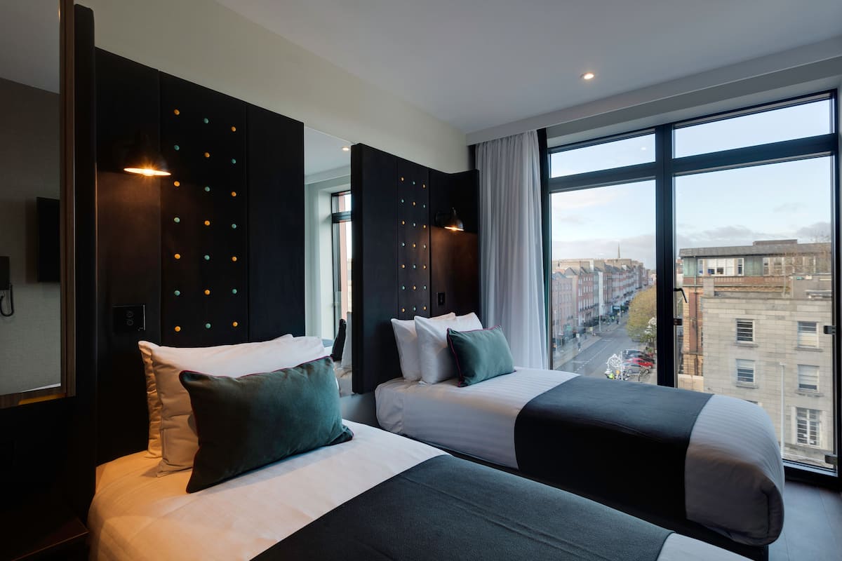 Une chambre d’hôtel moderne avec deux lits, de grandes fenêtres et une vue sur la ville.