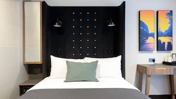 A modern hotel room with a bed, bedside lamps, a nightstand, and two paintings on the wall.