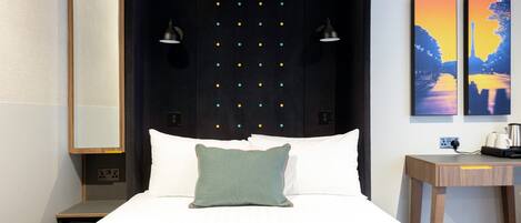 Quarto de hotel moderno com uma cama, abajures, mesa de cabeceira e duas pinturas na parede.