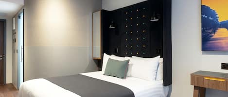 Una camera d'albergo moderna con un letto grande, una testiera scura e un comodino.