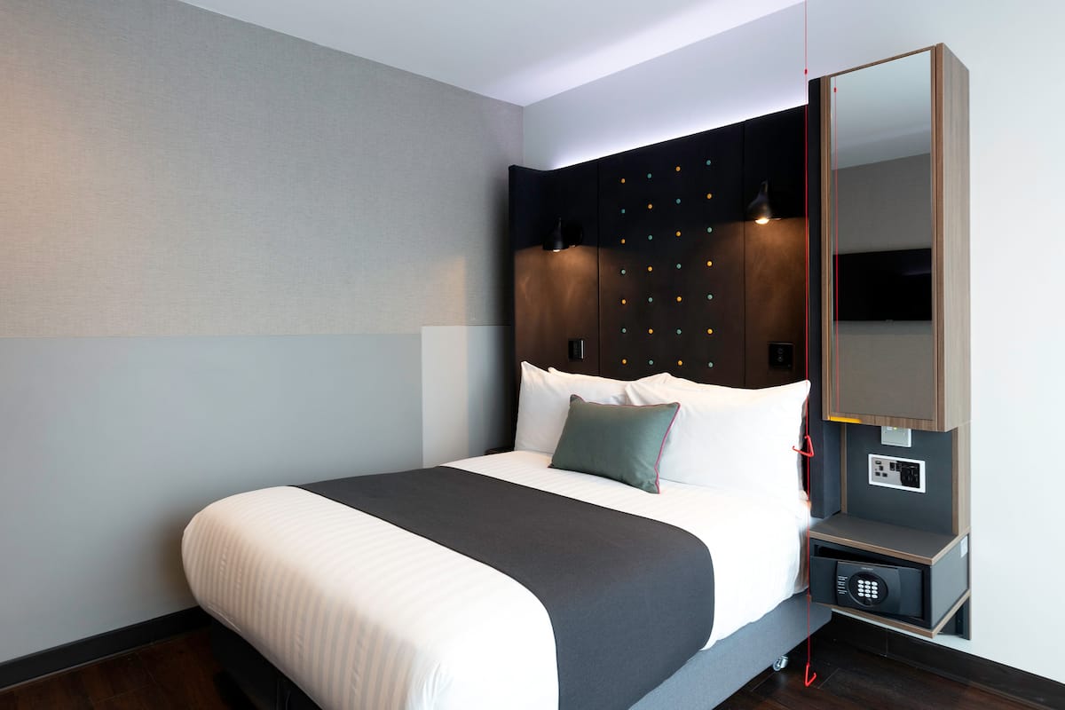 Une chambre d ’hôtel moderne avec un lit bien fait, une table de chevet avec une lampe et un coffre-fort intégré.