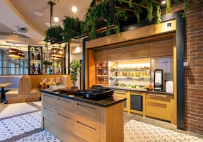 Una cocina moderna con armarios de madera, una isla central, plantas colgantes y una barra desayunadora.