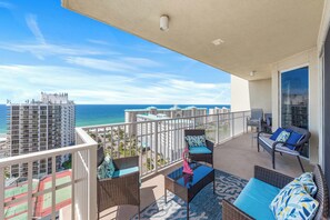 Ein Balkon mit Korbmöbeln, ein Tennisplatz und Blick auf das Meer und Gebäude.