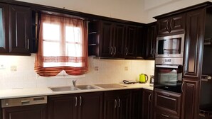 A kitchen with dark wooden cabinets, a stainless steel sink, a built-in oven, and a window with a striped curtain. - Antonis House (Sifnos)