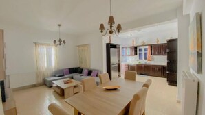 A modern living room with a wooden dining table and chairs, a grey sofa, and a kitchen in the background. - Antonis House (Sifnos)