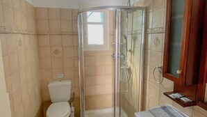 A bathroom with a glass-enclosed shower, a toilet, a sink, and a wooden cabinet. - Antonis House (Sifnos)