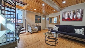 A spacious living room with a wooden ceiling, a glass coffee table, a dark sofa, patterned armchairs, and a painting of a forest. - Hill house 2 bedroom, 2 bath house. Walk to downtown Hill City, SD (Hill City)