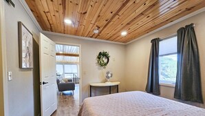A bedroom with a wooden ceiling, a bed with a patterned bedspread, a small table with a fan, and a window with curtains. - Hill house 2 bedroom, 2 bath house. Walk to downtown Hill City, SD (Hill City)