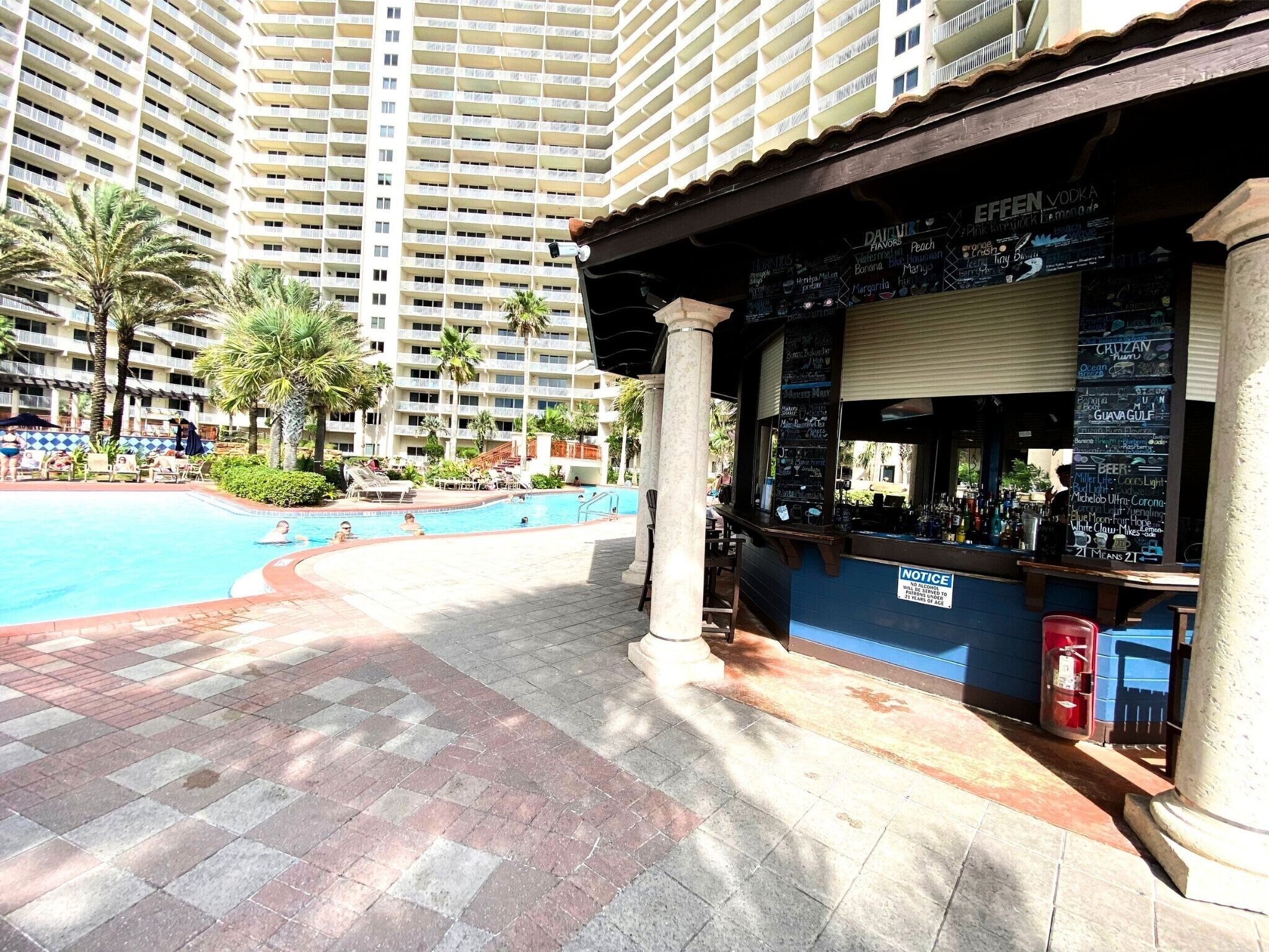 A bar area with a pool and palm trees in the background.