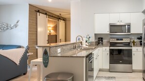 Una cocina moderna con armarios blancos, electrodomésticos de acero inoxidable, encimera de granito y una pequeña isla con un cubo de basura.