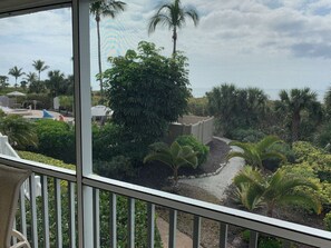A view from a balcony with a railing, overlooking a landscaped area with palm trees and a pool. - Gulf Beachfront 2BR Condo with Golf Privileges  (Sanibel)