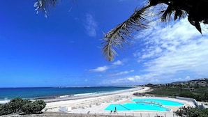 Vista da praia com piscina, céu claro e oceano.