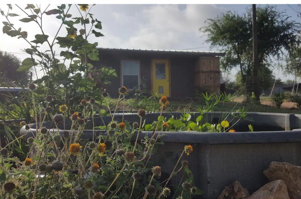 Una casa con puerta amarilla, rodeada de vegetación y una estructura de hormigón.