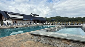 A swimming pool with lounge chairs and umbrellas, a stone wall, and a building with a metal roof. - Resort condo close to hiking and river/lake (Thornton)