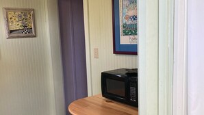 Une petite cuisine avec une table en bois et deux tabourets, un four à micro-ondes et une porte donnant sur une autre pièce.