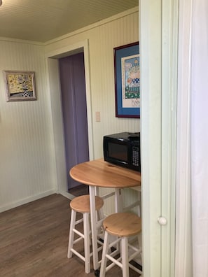 Compact kitchen area with a table, stools, microwave, and artwork.