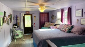 Une chambre à coucher comprenant un lit, une chaise, une porte avec un panneau indiquant la sortie, un ventilateur de plafond et une fenêtre avec des rideaux.
