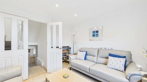 A living room with a sofa, a coffee table, and a door leading to a kitchen. - Solent Landing Beachfront Escape (Bembridge)