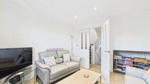 A living room with a sofa, a coffee table, a TV, and a bookshelf. - Solent Landing Beachfront Escape (Bembridge)