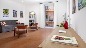 A modern living room with a grey sofa, wooden chairs, a wooden table with a magazine, and a red vase.