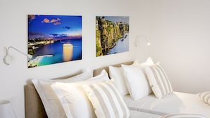 A neatly arranged bedroom with a bed, pillows, and two wall-mounted pictures depicting coastal scenes.
