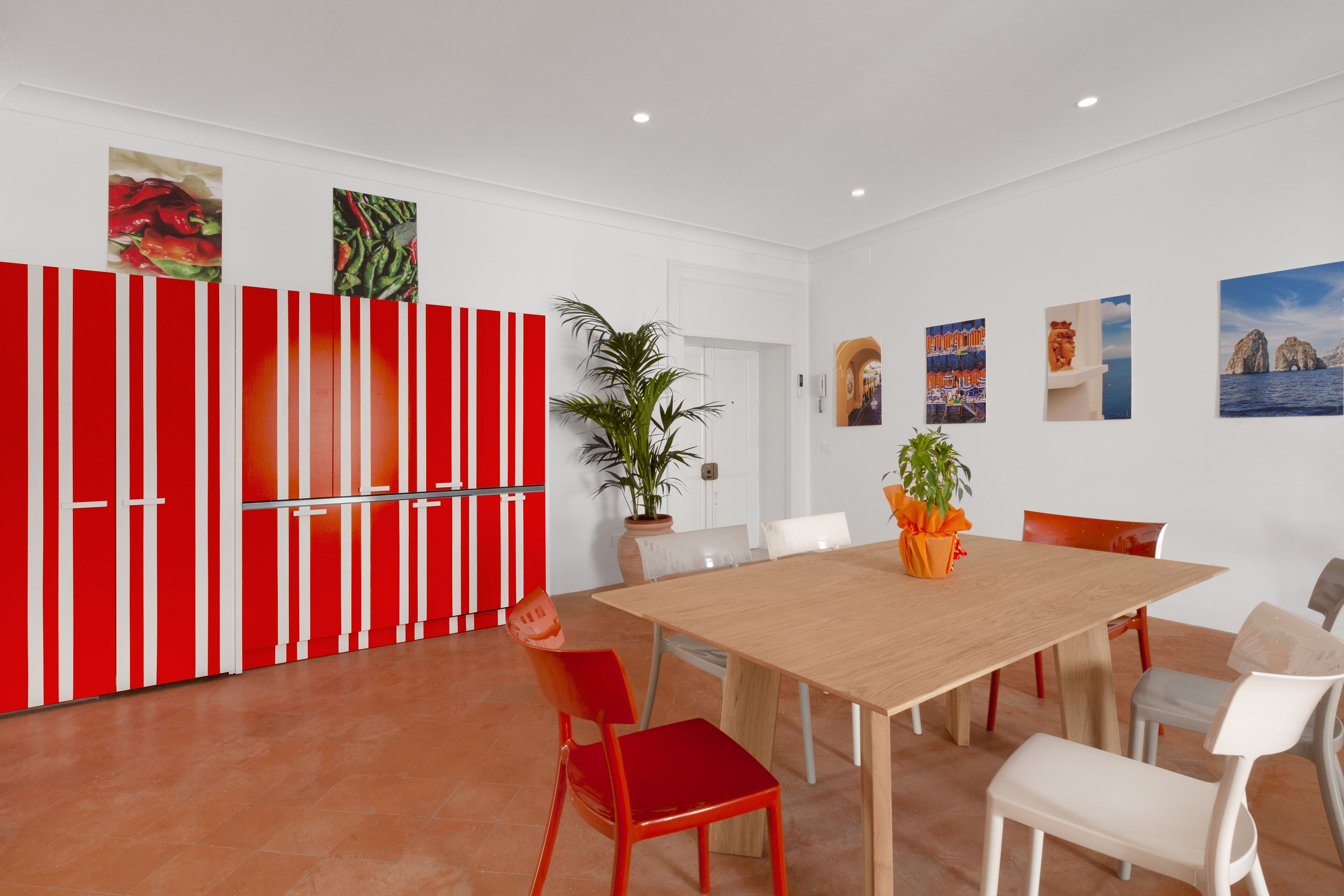 A modern dining area with a wooden table and chairs, a red and white striped cabinet, and various wall art.