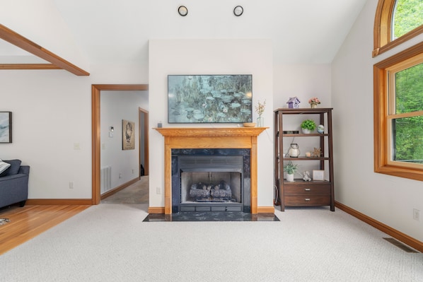 A spacious living room with a fireplace, a large painting above it, and a wooden bookshelf.