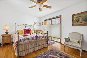 A bedroom with a bed, a chair, a ceiling fan, a window, and a painting on the wall. - Hamptons Beach House (East Hampton)