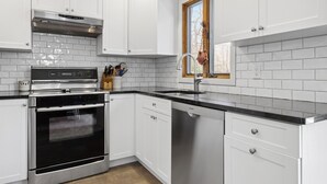 A modern kitchen with white cabinetry, stainless steel appliances, and a window with a view. - Hamptons Beach House (East Hampton)